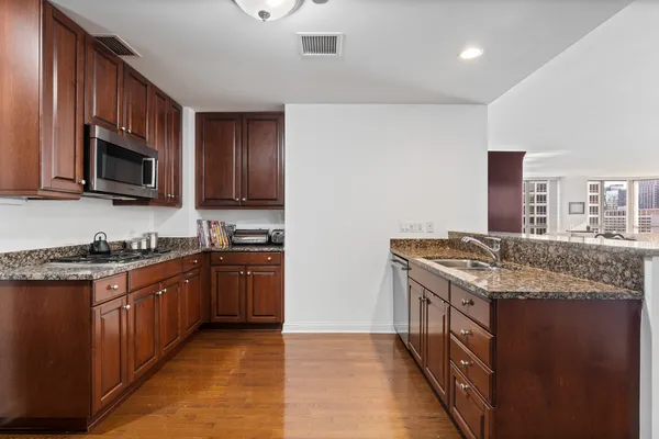 a kitchen with stainless steel appliances granite countertop a stove top oven a sink dishwasher and a microwave oven with wooden floor