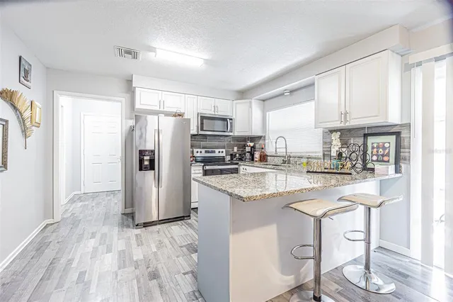 a kitchen with granite countertop a refrigerator a stove a sink and white cabinets with wooden floor