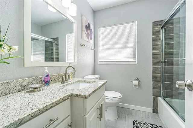 a bathroom with a granite countertop sink a toilet a mirror and shower
