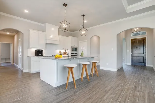 a kitchen with stainless steel appliances granite countertop a kitchen island a stove a refrigerator a sink a dining table and chairs with wooden floor