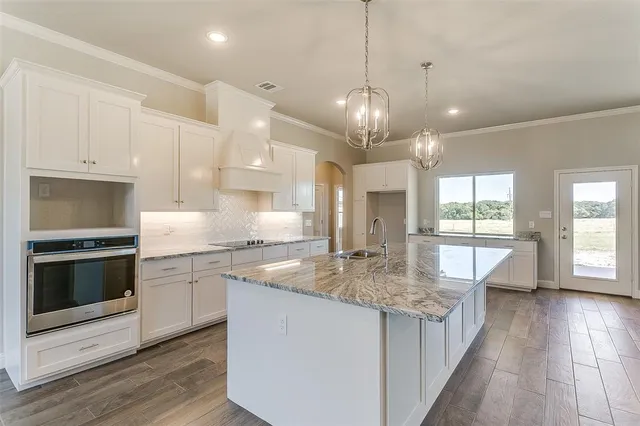 a kitchen with kitchen island granite countertop a stove a sink and white cabinets with wooden floor