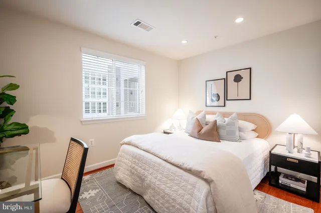 a bedroom with a bed a chair and potted plant on the dresser
