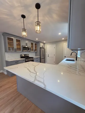 a large kitchen with stainless steel appliances a large counter top a stove and a sink with chandelier