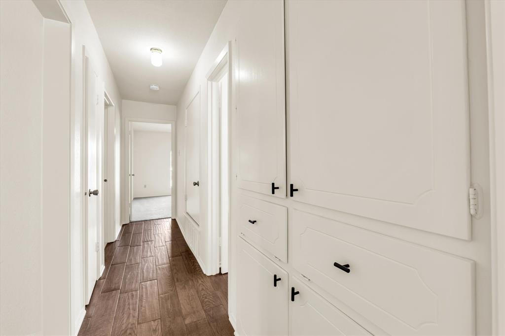 141 Travis Lane Hewitt, TX 76643 - Photo 13 of 31 Hallway featuring wood-finish flooring, white walls, and built-in white cabinetry with black hardware