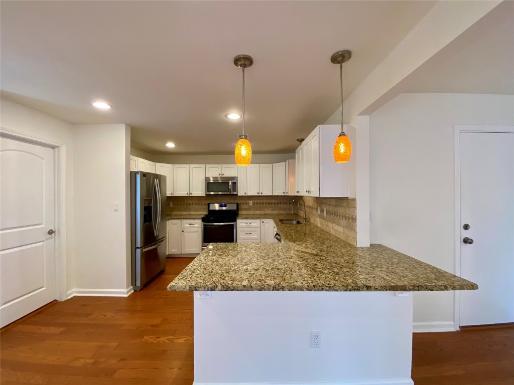 2003 Patton Lane Austin, TX 78723 - Photo 9 of 38 Kitchen with appliances with stainless steel finishes, decorative light fixtures, a peninsula, dark stone counters, and white cabinetry