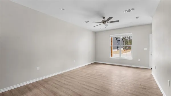 an empty room with wooden floor ceiling fan and windows