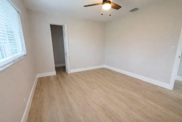 an empty room with wooden floor fan and window