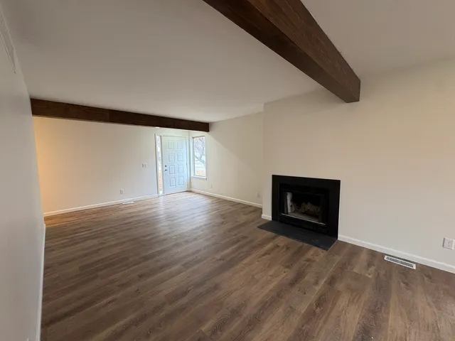 a view of an empty room with wooden floor fire place and a window