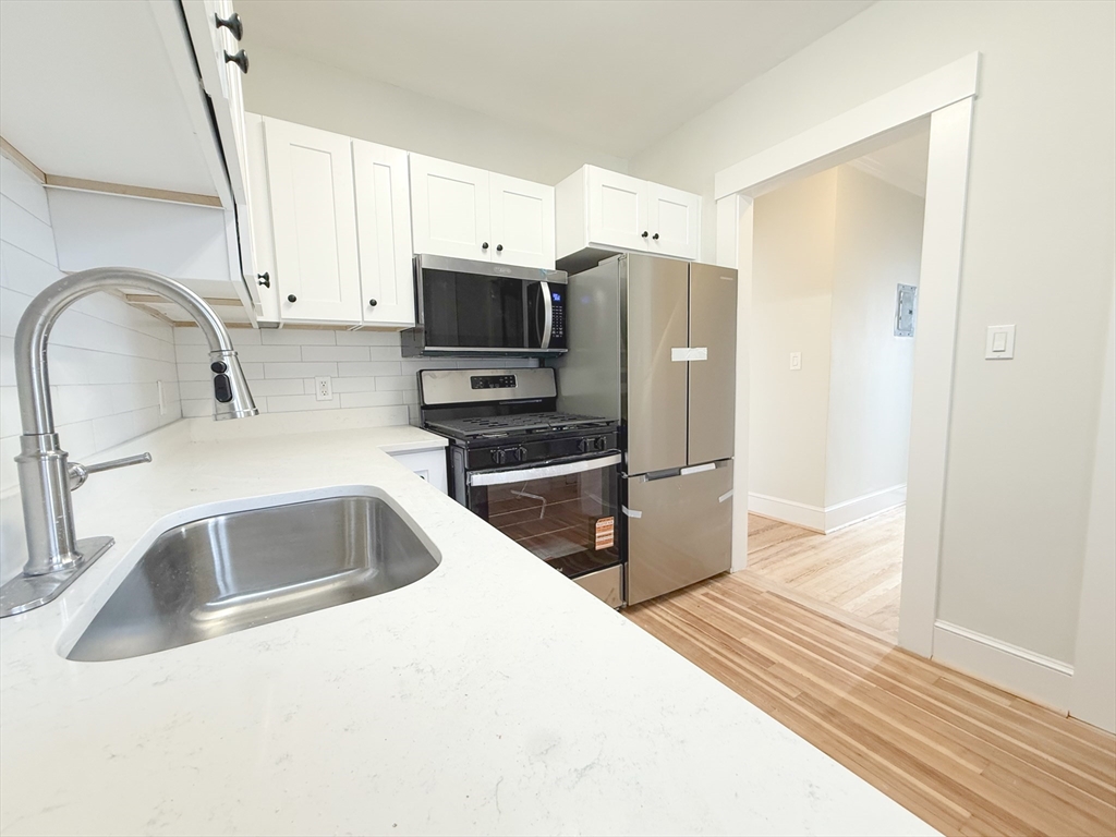 56 Selkirk Road, Unit 8 Boston, MA 02135 - Photo 4 of 8 a kitchen with stainless steel appliances a sink a stove and a refrigerator with wooden floor