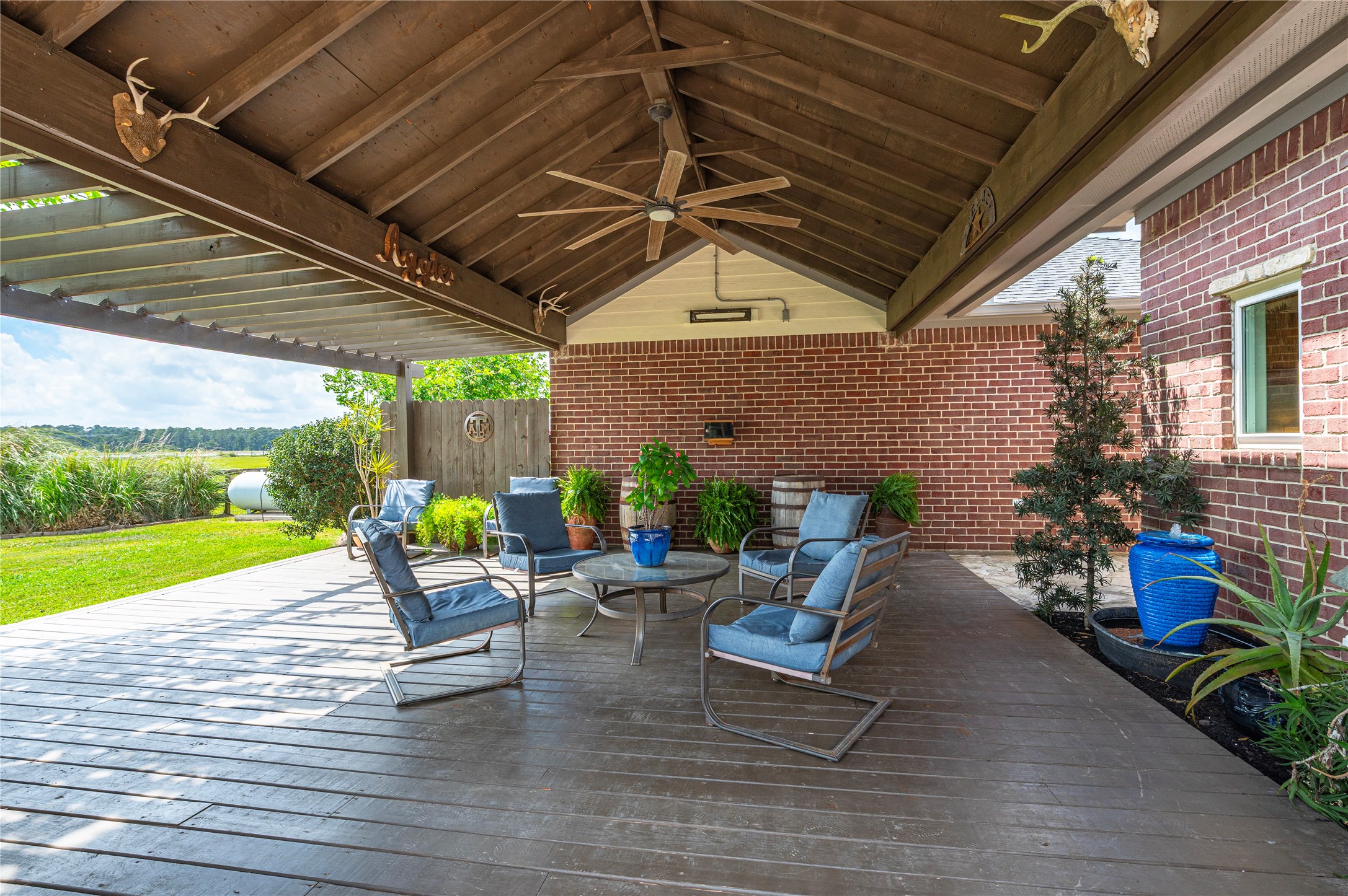 8211 Deats Lane Dickinson, TX 77539 - Photo 21 of 50 Backyard entertainment area surrounded by lush landscaping and quipped with a large wood decked patio, ceiling fan, and TV outlet, perfect for outdoor dining and gatherings.