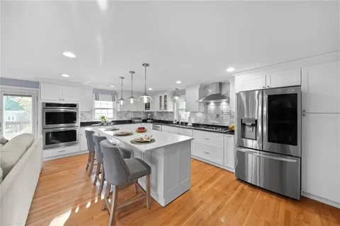 a kitchen with stainless steel appliances granite countertop a refrigerator a stove top oven a sink dishwasher and white cabinets with wooden floor