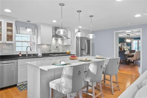a kitchen with stainless steel appliances granite countertop a sink a stove a dining table and chairs