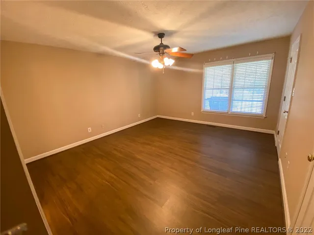 an empty room with wooden floor fan and windows