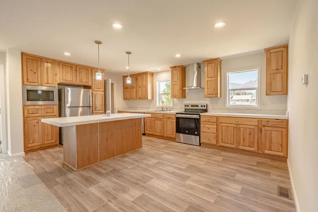 a large kitchen with stainless steel appliances kitchen island granite countertop a stove a sink a refrigerator and white cabinets with wooden floor