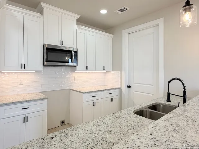 a kitchen with granite countertop a stove a sink and white cabinets with wooden floor