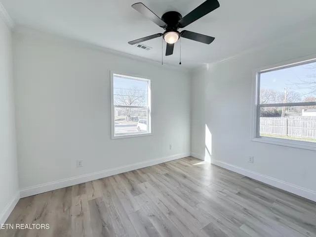an empty room with wooden floor ceiling fan and windows