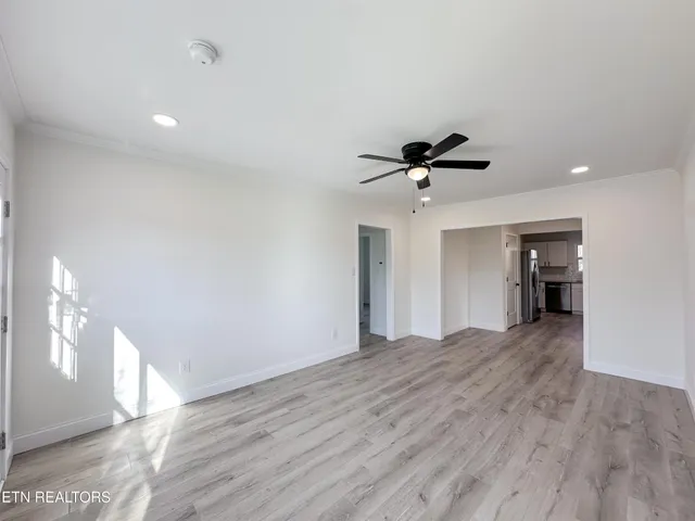 a view of an empty room with wooden floor and a ceiling fan