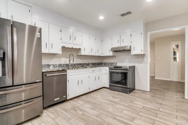 a kitchen with granite countertop white cabinets and stainless steel appliances