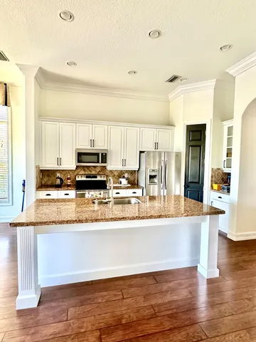 a large kitchen with stainless steel appliances granite countertop a refrigerator a stove and a wooden floors