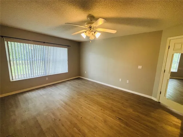 an empty room with wooden floor fan and windows