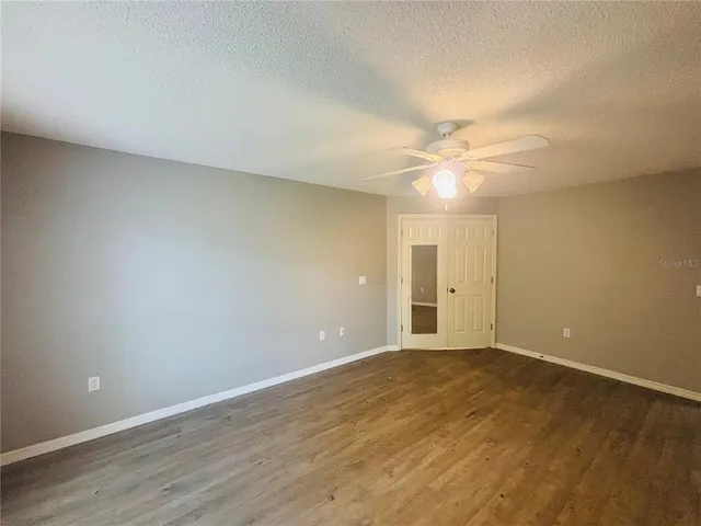 a view of an empty room with wooden floor and a ceiling fan