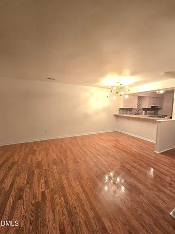an empty room with wooden floor and kitchen view