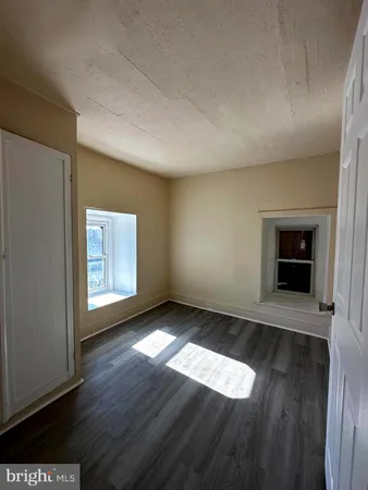 an empty room with wooden floor fireplace and windows