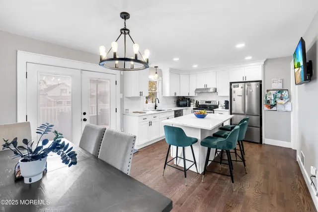 a kitchen with stainless steel appliances kitchen island granite countertop a dining table chairs and white cabinets