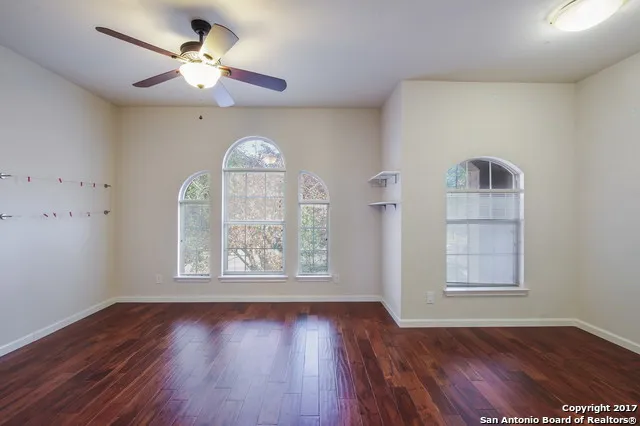 an empty room with wooden floor chandelier fan and windows