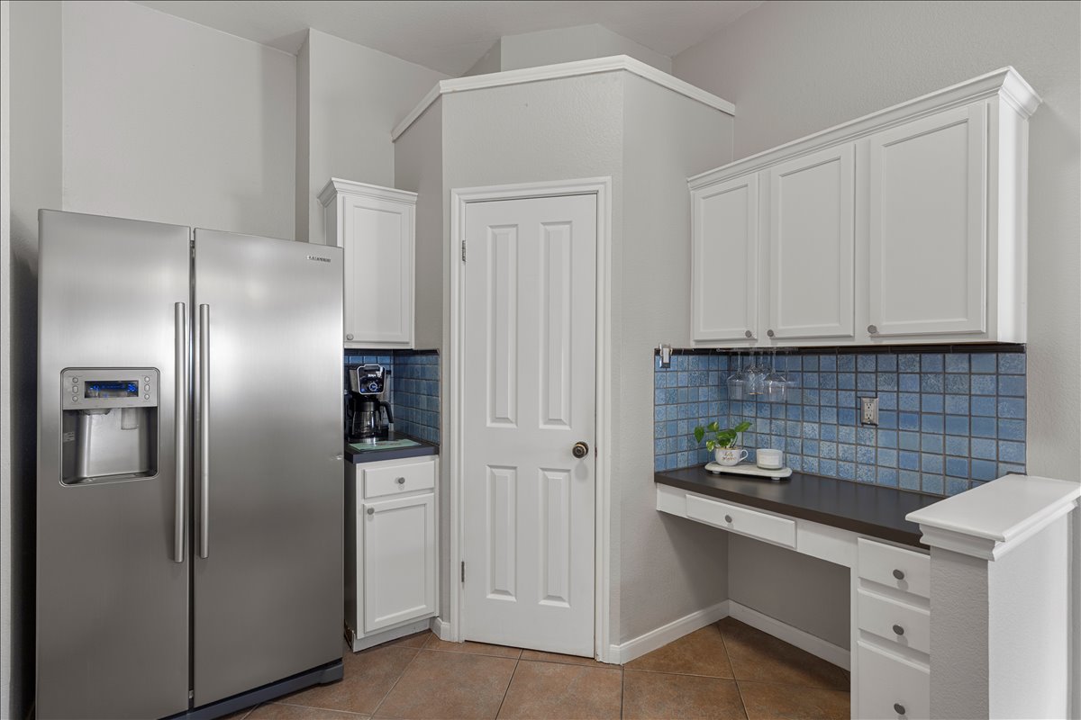 9012 Meacham Way Austin, TX 78749 - Photo 10 of 34 Kitchen area featuring a stainless steel side-by-side refrigerator, white cabinetry with crown molding, blue tile backsplash, a built-in desk, and a wine glass rack