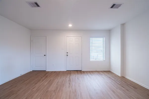 a view of an empty room with wooden floor and window