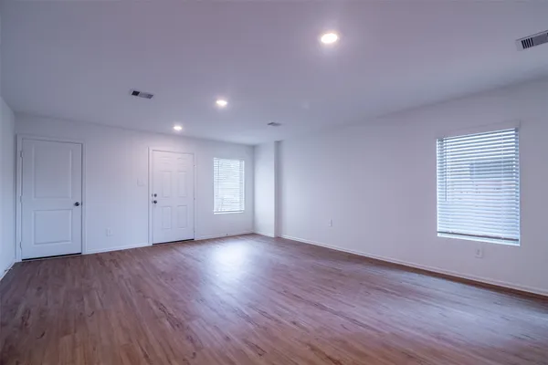 a view of an empty room with wooden floor and a window
