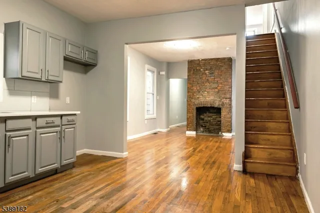 a view of an empty room with wooden floor and a kitchen