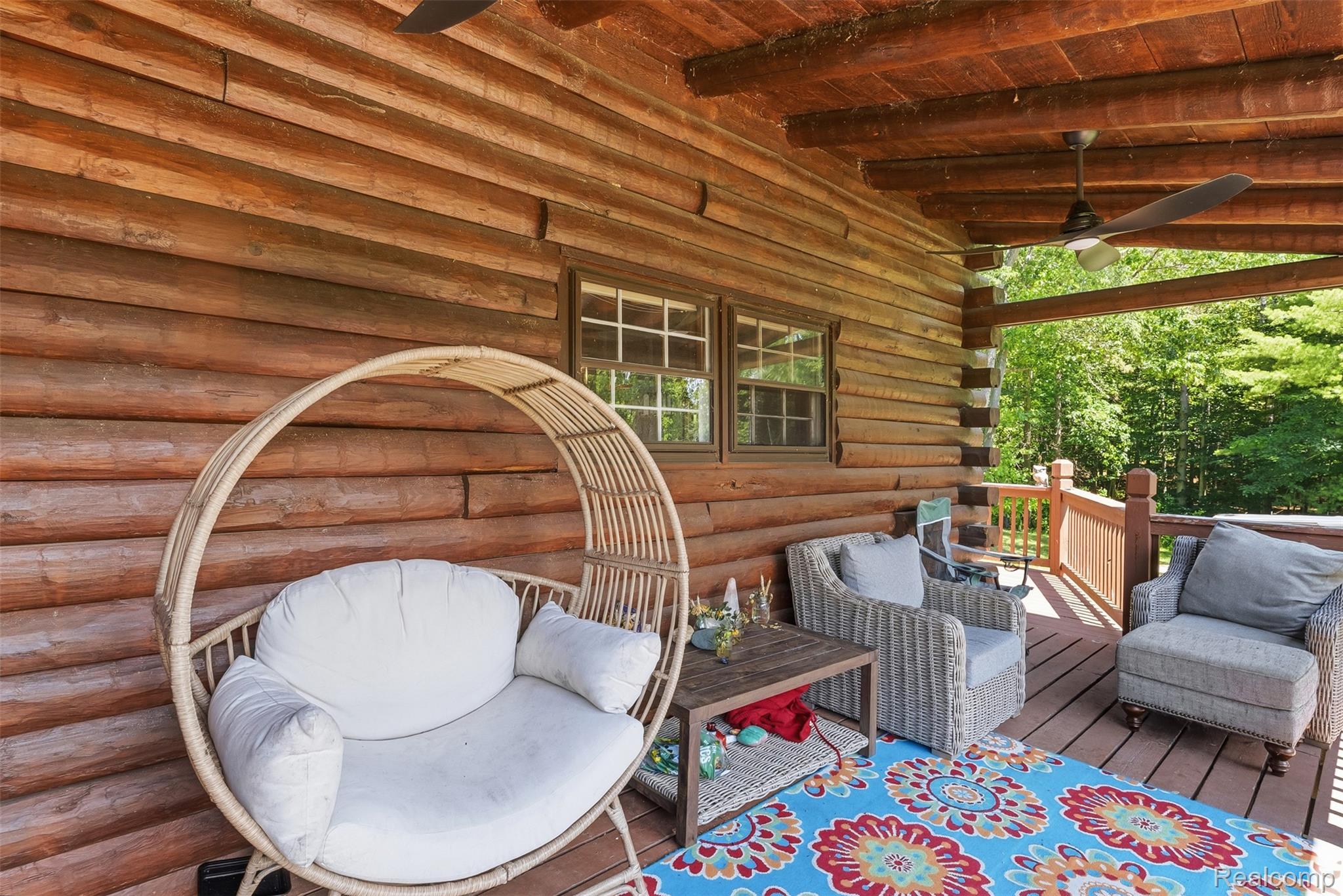 3656 Stanley Road Columbiaville, MI 48421 - Photo 45 of 65 Covered porch featuring a log cabin exterior, exposed wood beam ceiling, wood-finish flooring, and a forest backdrop