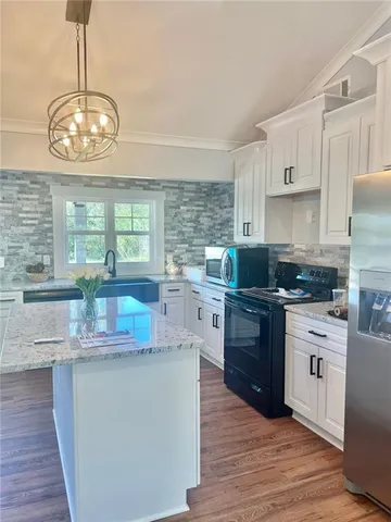 a kitchen with stainless steel appliances granite countertop a stove top oven a sink dishwasher a refrigerator and white cabinets with wooden floor