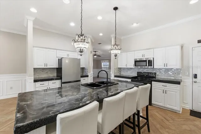 a kitchen with stainless steel appliances granite countertop a stove a sink a refrigerator a center island a stove and white cabinets with wooden floor