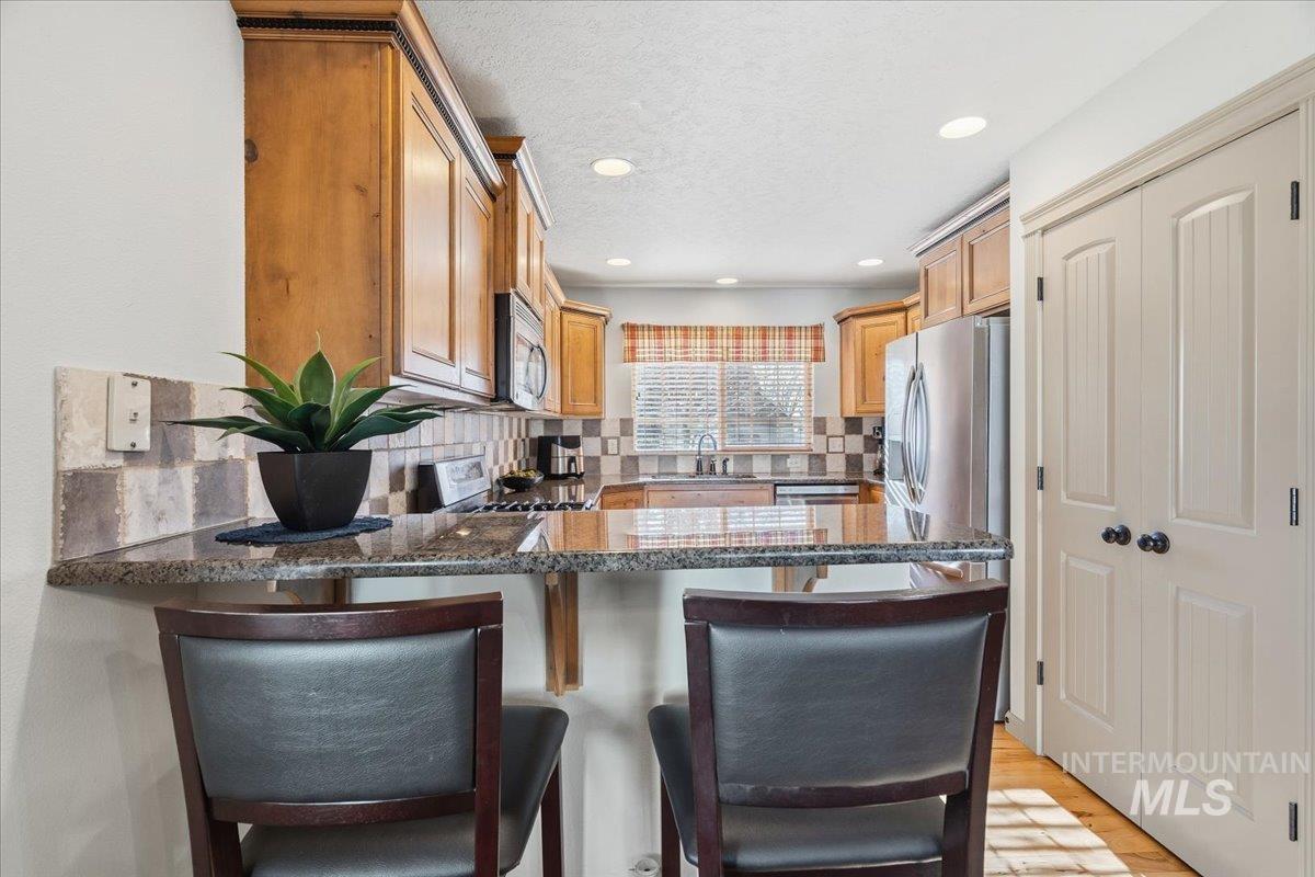 679 North Shadowfox Place Eagle, ID 83616 - Photo 14 of 28 Kitchen with a peninsula, dark stone counters, a kitchen breakfast bar, stainless steel appliances, and a textured ceiling