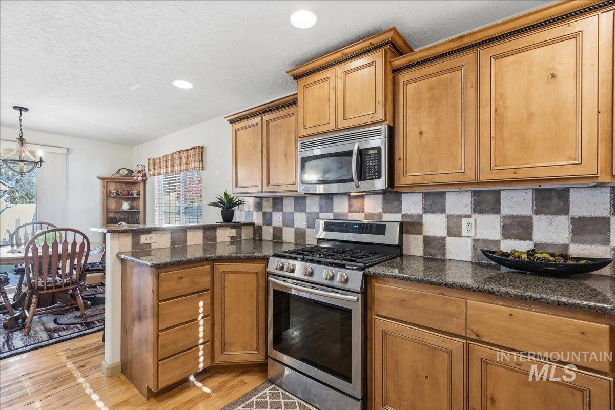 679 North Shadowfox Place Eagle, ID 83616 - Photo 15 of 28 Kitchen with stainless steel appliances, a peninsula, brown cabinets, a textured ceiling, and tasteful backsplash