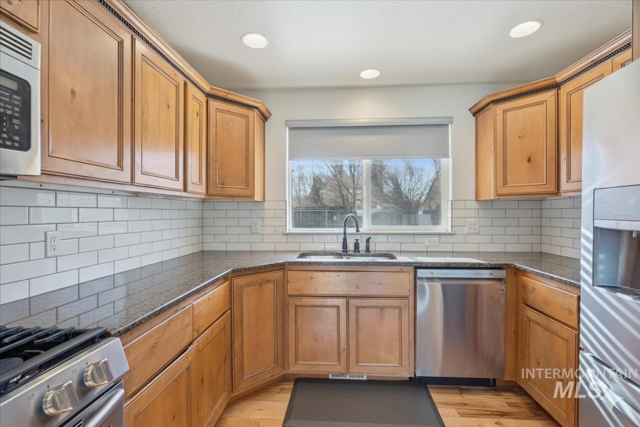 679 North Shadowfox Place Eagle, ID 83616 - Photo 5 of 28 Kitchen with stainless steel appliances, dark stone countertops, light wood-style flooring, and backsplash