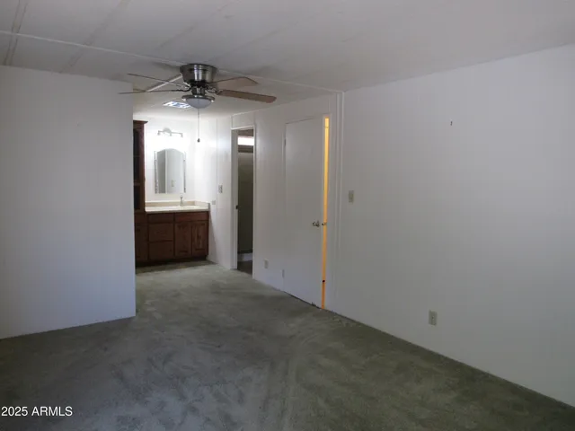 an empty room with chandelier fan and kitchen view