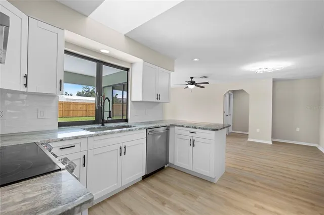 a kitchen with a sink dishwasher a stove and white cabinets with wooden floor