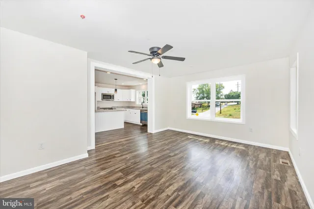 an empty room with wooden floor chandelier fan and windows