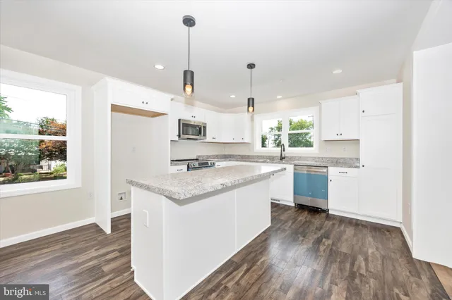 a kitchen with stainless steel appliances granite countertop a sink a stove a refrigerator and island with wooden floor