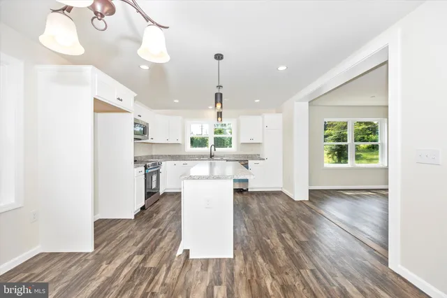 a view of a kitchen with kitchen island wooden floors stainless steel appliances and a window