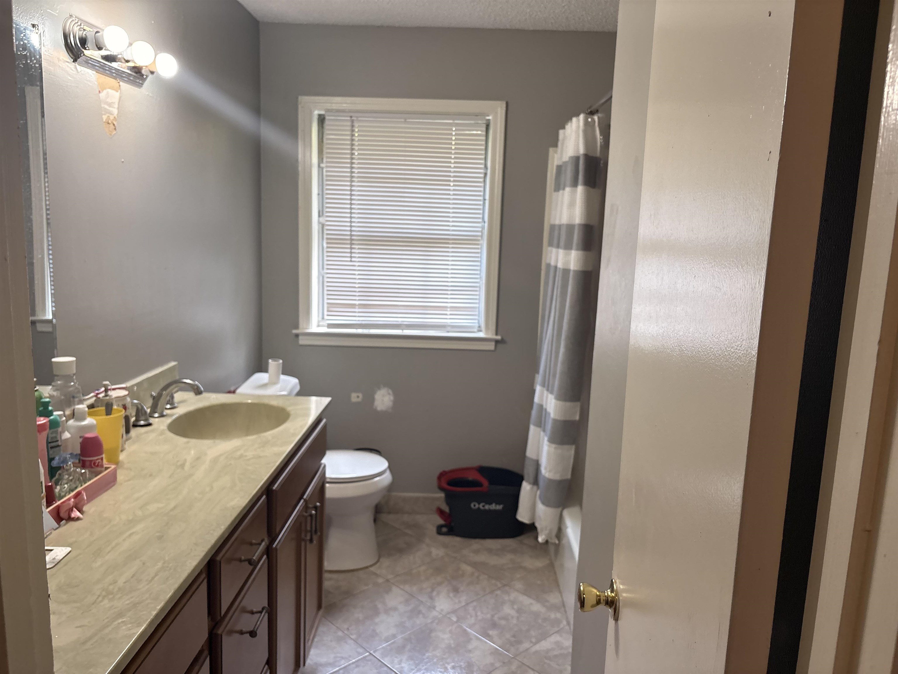 4009 Tessland Road Memphis, TN 38128 - Photo 11 of 16 Bathroom featuring a single vanity with wood-finish cabinetry and a light-toned countertop, a window with blinds, a toilet, a built-in bathtub with shower, and tiled flooring