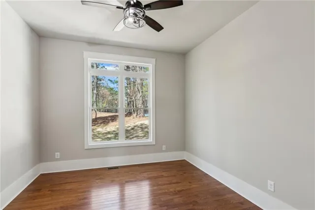 an empty room with wooden floor fan and windows