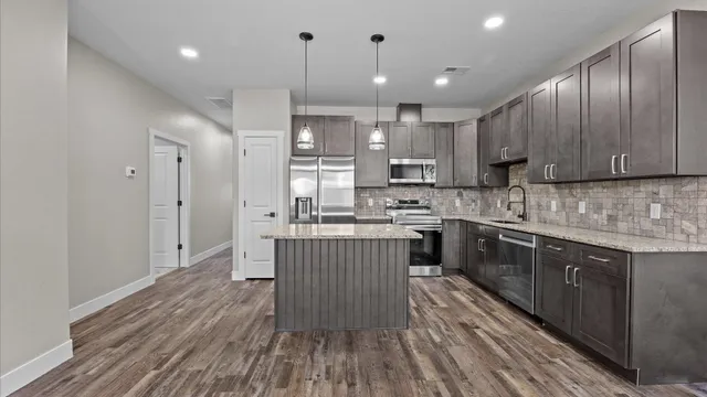 a kitchen with kitchen island granite countertop wooden floors wooden cabinets and stainless steel appliances