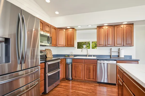 a kitchen with stainless steel appliances granite countertop a refrigerator a sink dishwasher a stove and white countertops with wooden floor