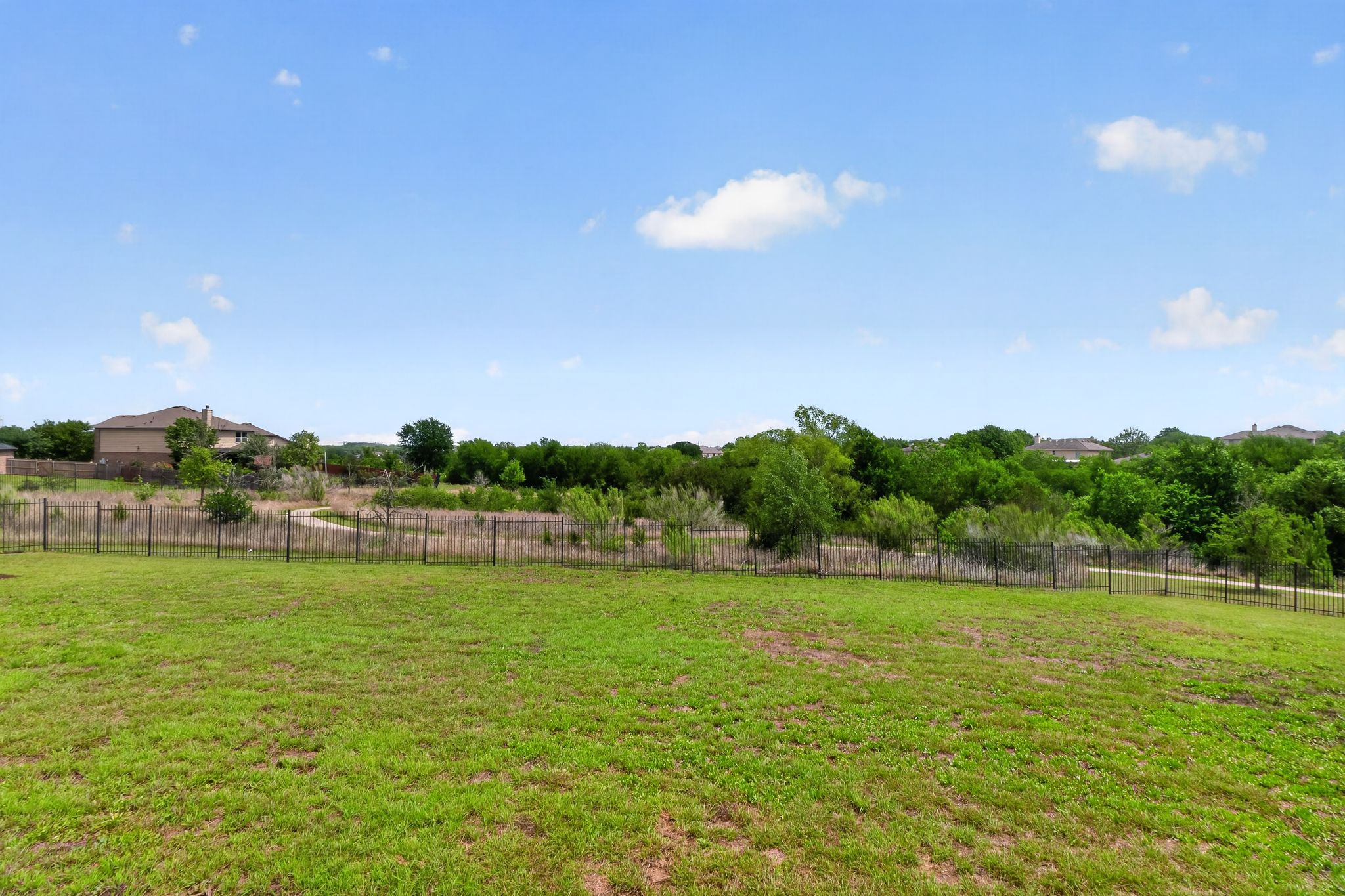 5816 Minch Road Austin, TX 78754 - Photo 14 of 15 The property features a spacious grassy yard with a black metal fence, overlooking a natural area with trees and a visible dirt path