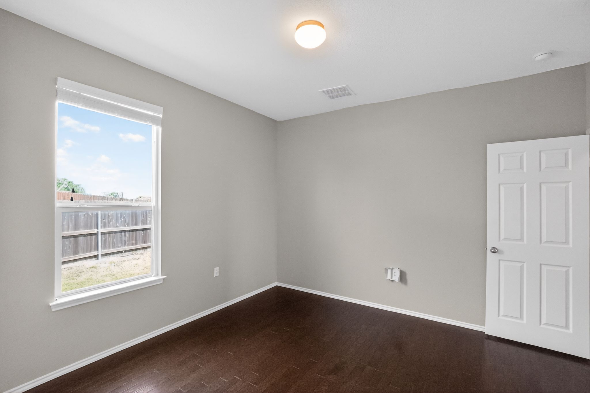 5816 Minch Road Austin, TX 78754 - Photo 4 of 15 Bright room featuring dark wood flooring, light grey walls, white trim, a white six-panel door, and a single window with a privacy blind